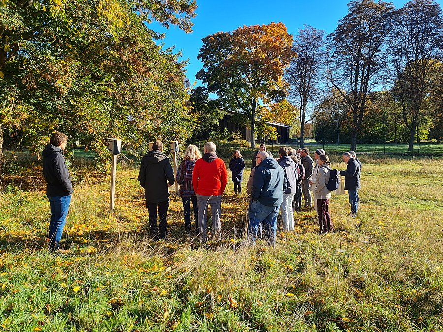 Viele Personen von hinten auf dem Feld vor einer Wildbienennisthilfe