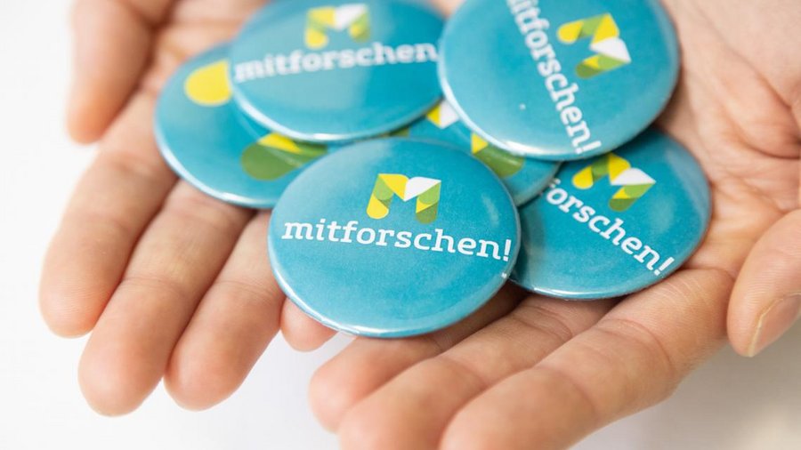 Zwei offene Händen halten mehrere Buttons mit der Aufschrift mitforschen