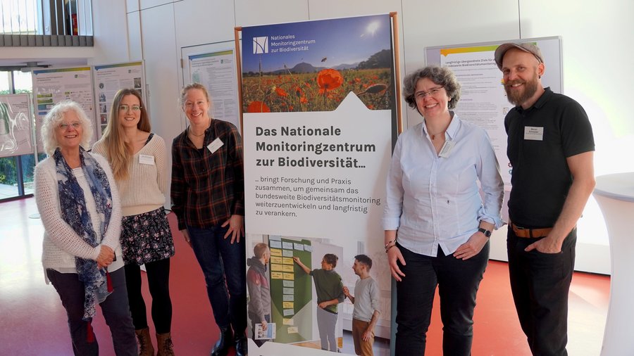 fünf Personen vor einer Fahne des Nationalen Monitoringzentrum
