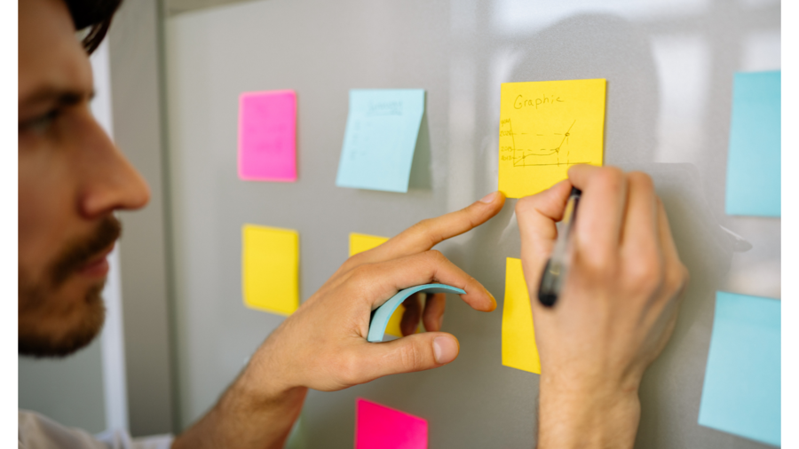 Man writes notes on a post it sticked to pinboard.